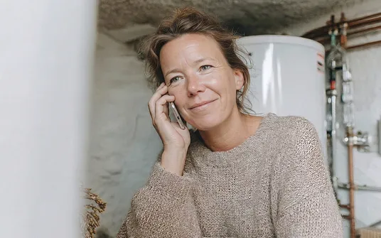 Frau ruft per Telefon den Service für Ihre Heizung.